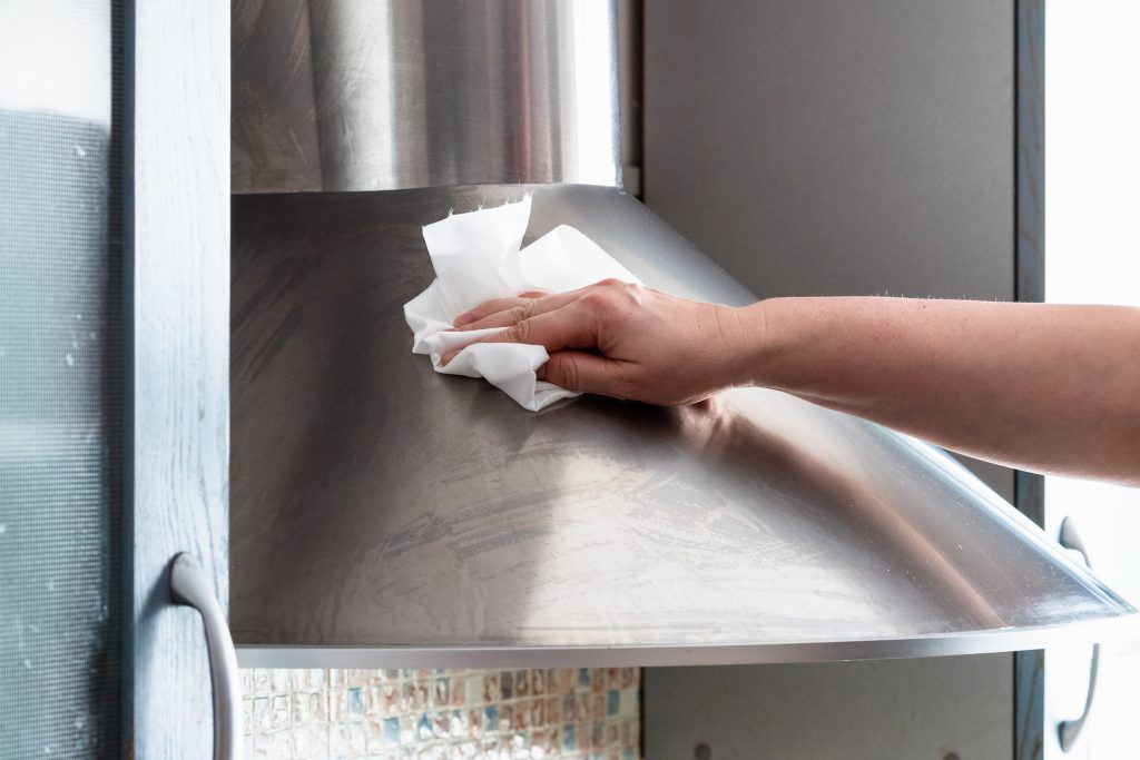 A lady wiping a stainless steel surface dry with a kitchen napkin.