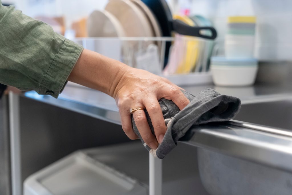 A lady wiping down a stainless steel counter with a dry cloth
