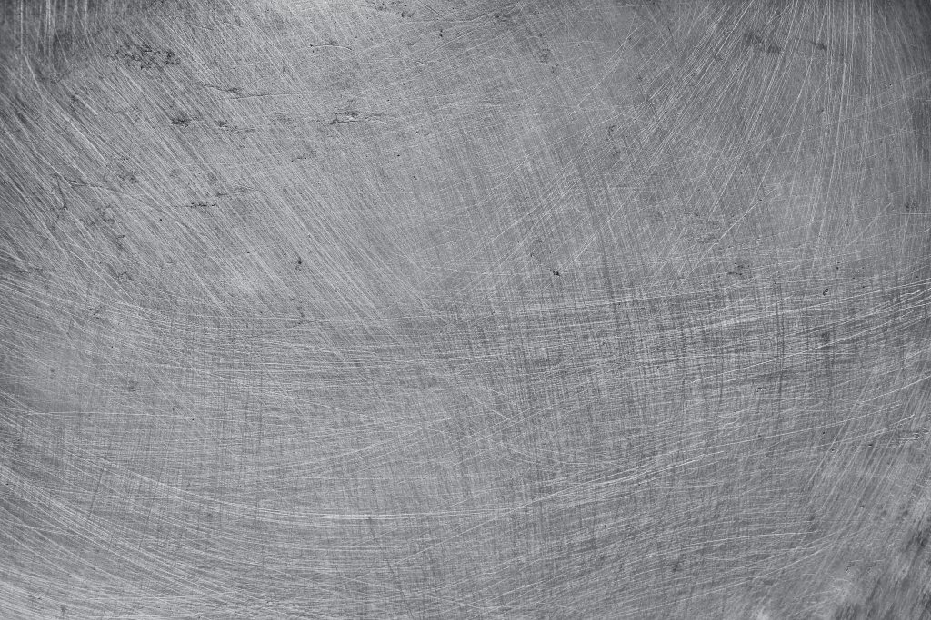 A stainless steel surface with irregular brush strokes resulting from brushing against the grain.